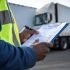 closeup-persons-hand-holding-pen-writing-clipboard-wearing-safety-reflective-vest-with-delivery-vehicle-background_132358-40700